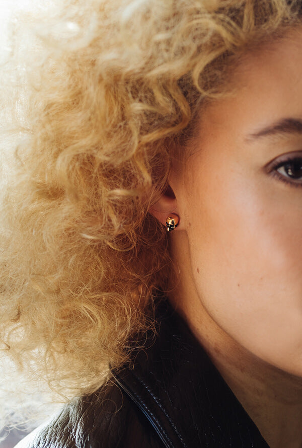 The side of a womens face with blond curly hair. She is wearing silver skull stud earrings.